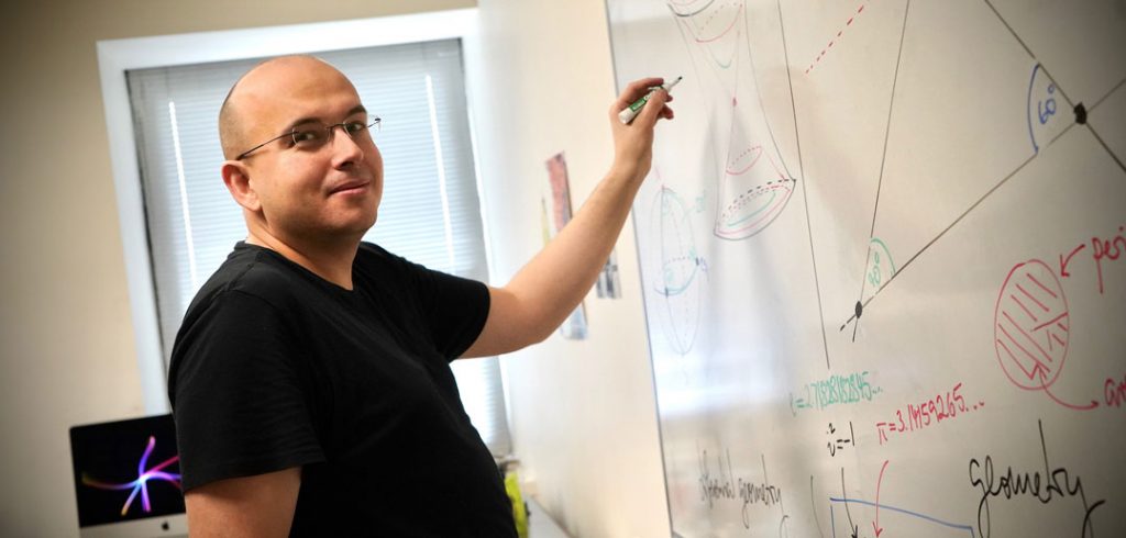 A man holds a marker by a whiteboard that has math equations on it.