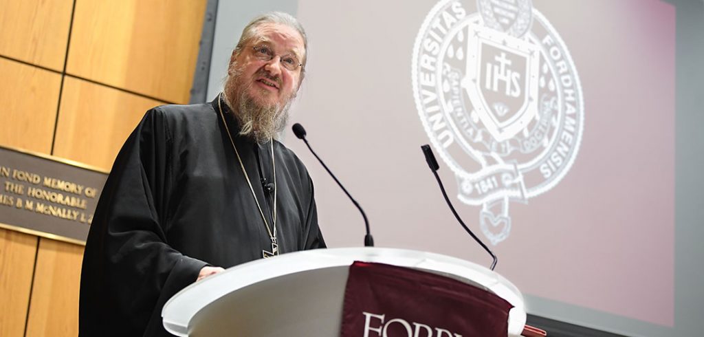 Father John Behr speaks at a podium in black clerical robe