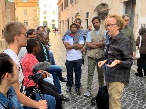 A man speaking with a group of students on a street