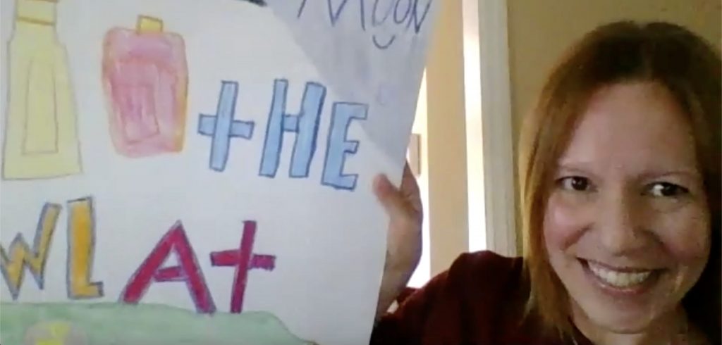 A woman holds a poster in front of a camera.