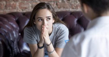 A young woman sits forward with her hands pressed together.