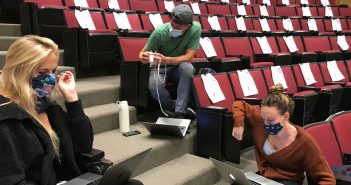 Three students sit spaced out in an auditorium