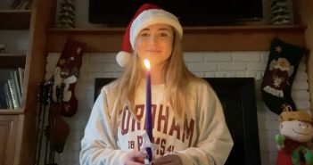 Passing the Light: A Holiday Message of Hope A young woman wearing a red Santa hat holds a taper candle and smiles at the camera.