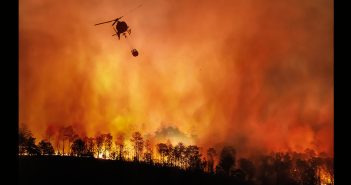A helicopter flying above a burning landscape