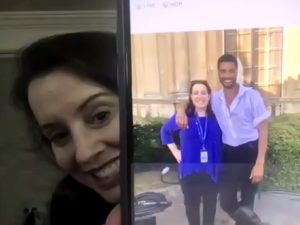 A woman holds a phone screen in front of her. The screen shows a photo of a couple.