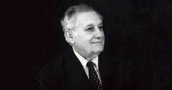 A black and white photo of an elderly man wearing a tie and smiling off into the distance