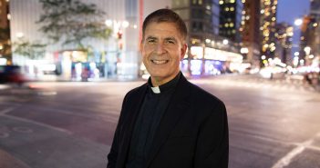 Father John Cecero in Columbus Circle at dusk, with streetlights