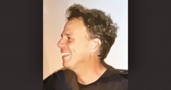 A side profile of a smiling man wearing a black shirt