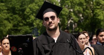 A Graduate Who Overcame a Car Accident That Changed His Life A man wearing sunglasses and a black graduation cap and gown smiles.