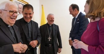 Five standing people laugh at someone's comment.