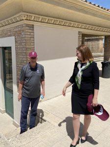 A woman holding a maroon baseball cap smiles as a man poses with a maroon baseball cap on his head.