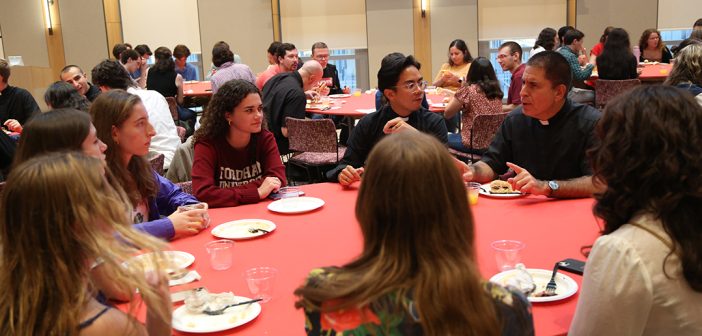 Father Cecero chatting with students at round table at reception