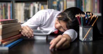 What Time Should School Really Start? Student teen sleeping sit at table at library study online on laptop with textbook