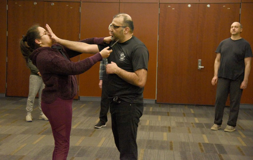 A man puts his arm in a woman's face while she holds a knife to his throat.