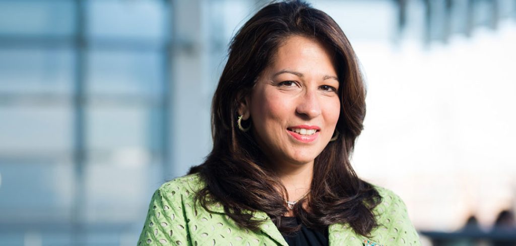 A woman in a light-green business suit and black top smiles at the camera