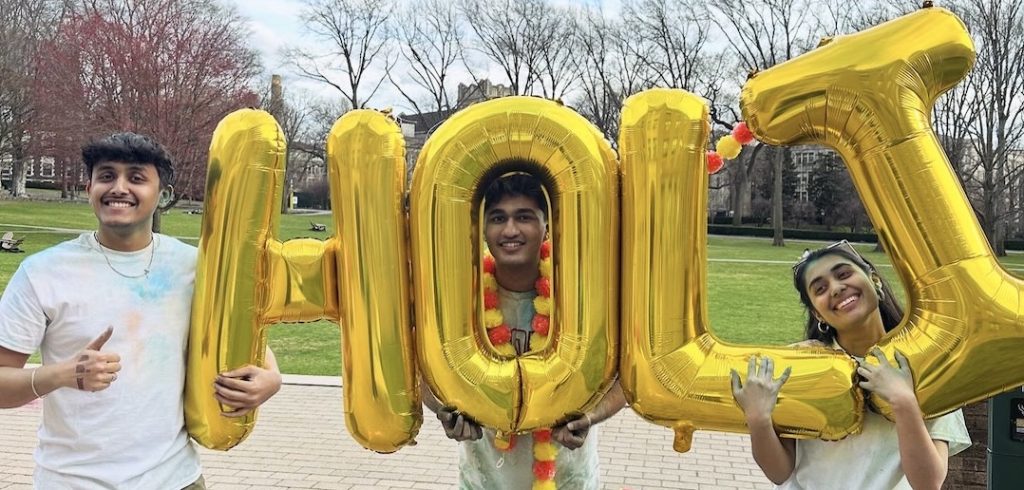 Three students hold jumbo gold balloons that spell out "HOLI."