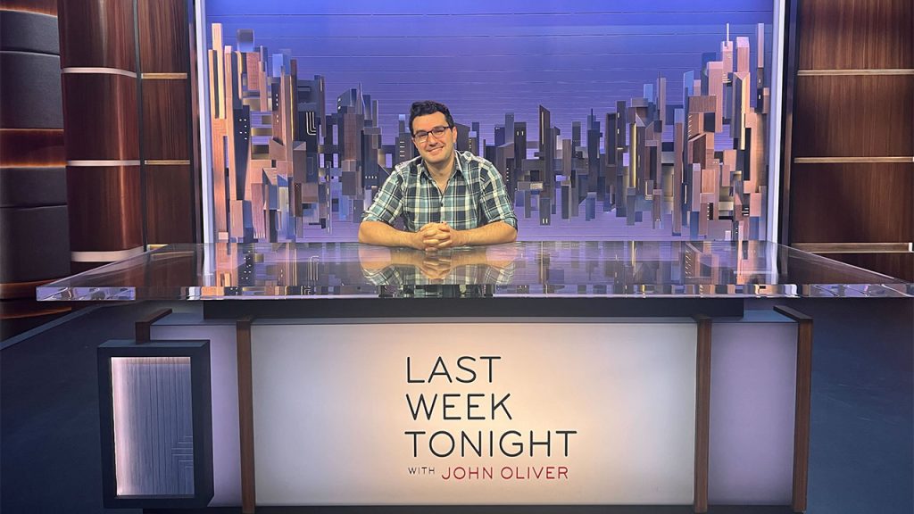 Seena Vali sitting at the desk on set of Last Week Tonight.