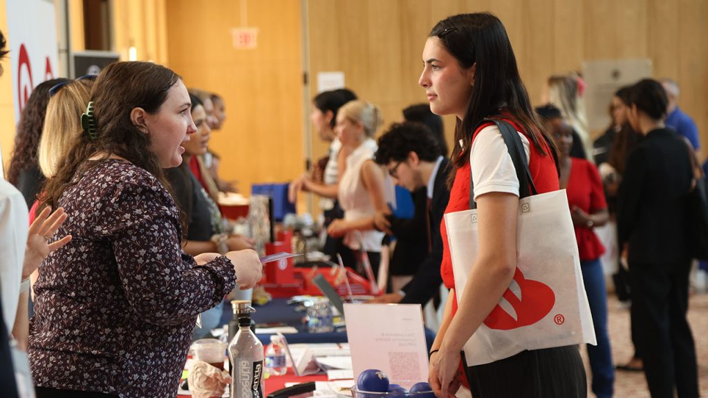 Fordham Announces Internship Promise A female student speaks to an older woman standing behind a table.