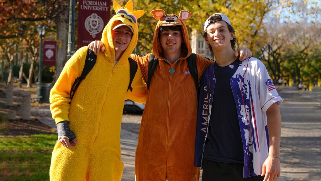 Student in Big Bird onesie (left), student in Scooby Doo onesie (center), and student in baseball outfit (right).