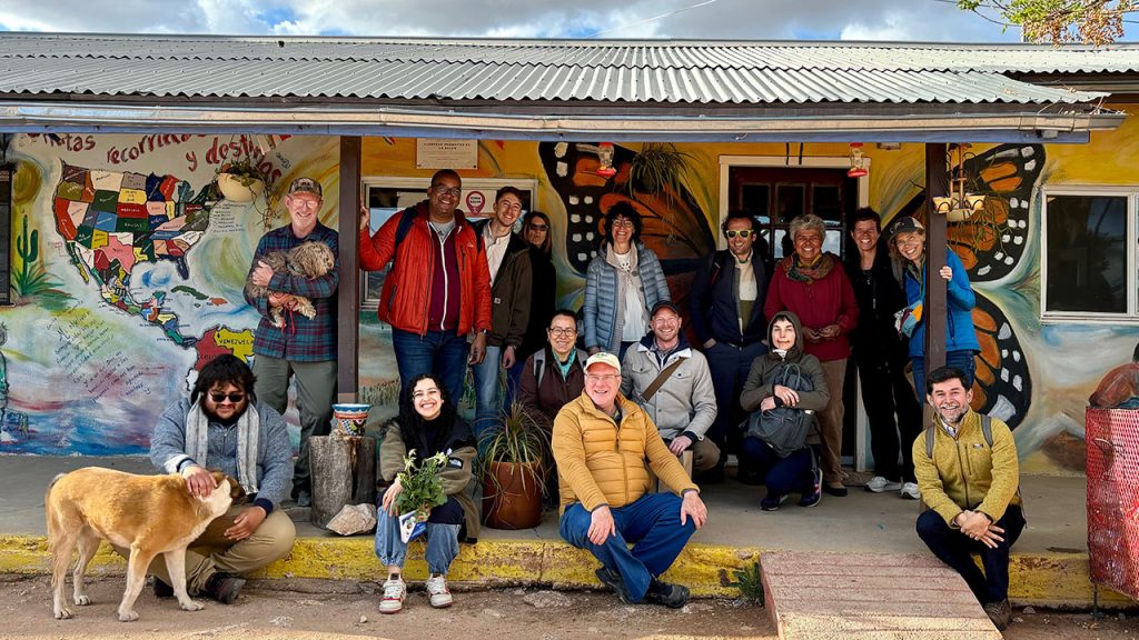 A group of Fordham professors standing and sitting together in front of a building with a colorful mural.