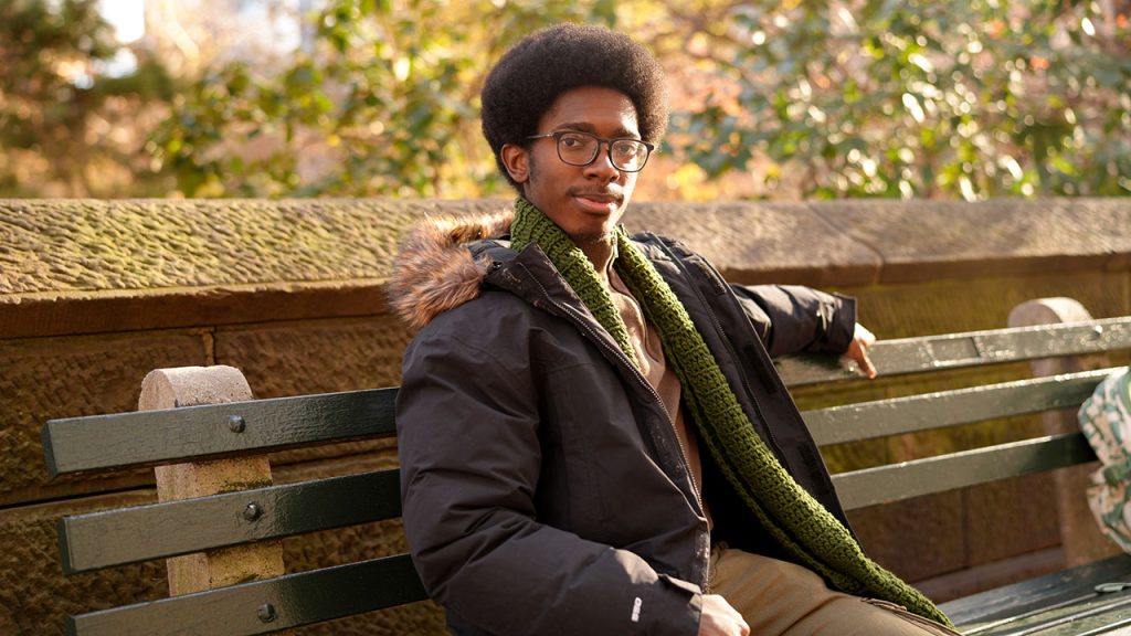 Student Intern Helps Fordham Combat Climate Change A man sitting on a bench with his arm extended.
