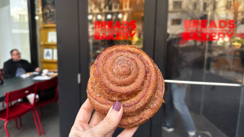 A woman holds a pastry in her hand from Breads Bakery