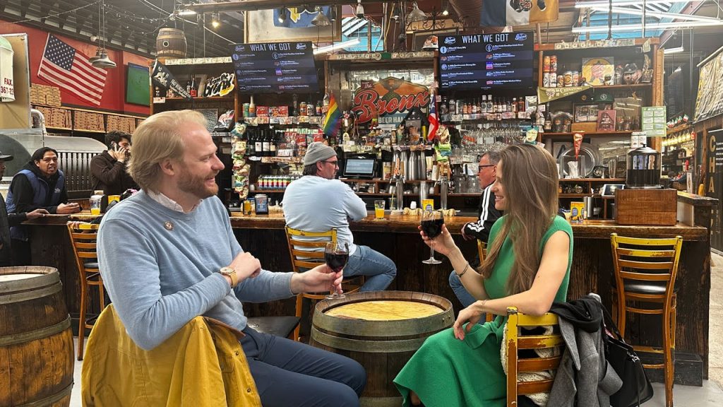 Two people hold glasses of wine in a "cheers" position at Bronx Beer Hall, representing the best spots to eat and drink near Fordham's Rose Hill campus.