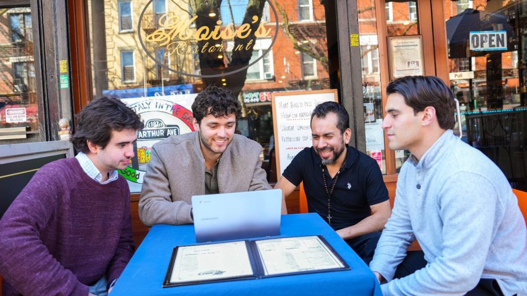 Four men sit around a table outside of Moise's Restorante in the Bronx, as part of an outing for Fordham's Consult Your Community Club.