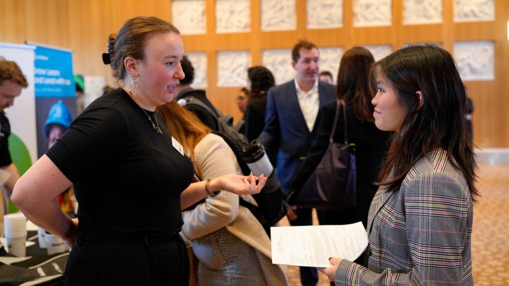 A young woman holds her resume while chatting with another woman at a career fair at Fordham