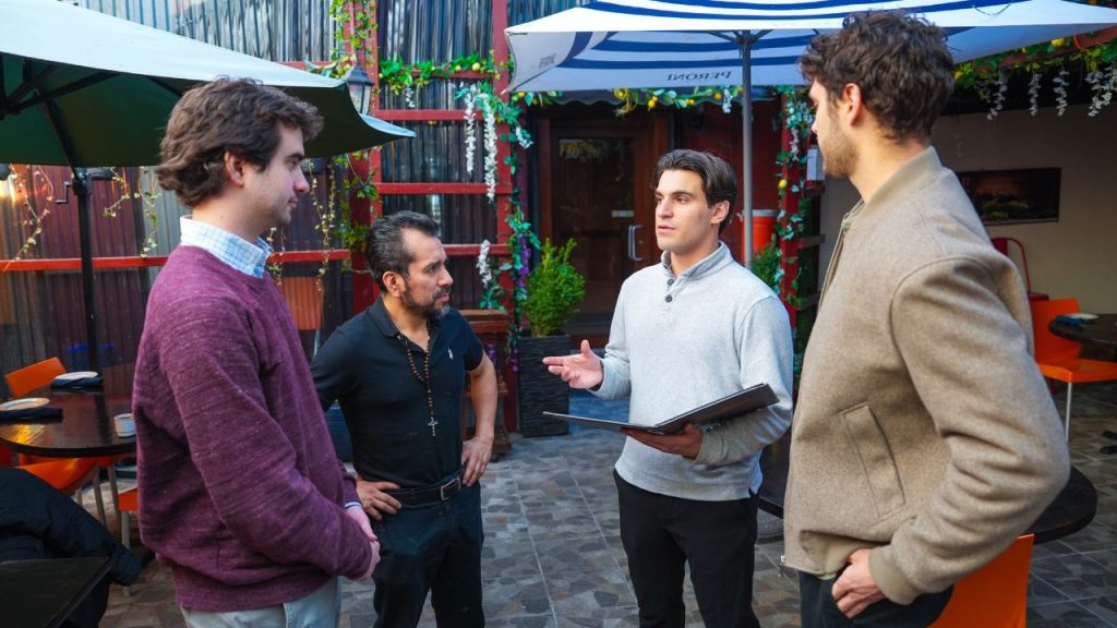 Four men stand on a patio chatting outside of Moise's Ristorante in the Bronx as part of Fordham's Consult Your Community Club 