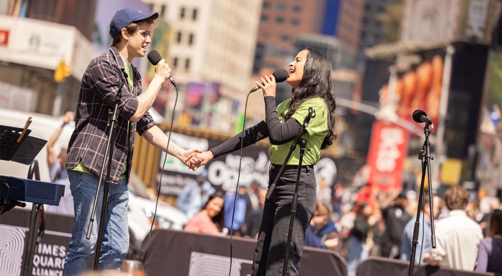 Man and woman holding hands on stage singing to each other, holding microphones
