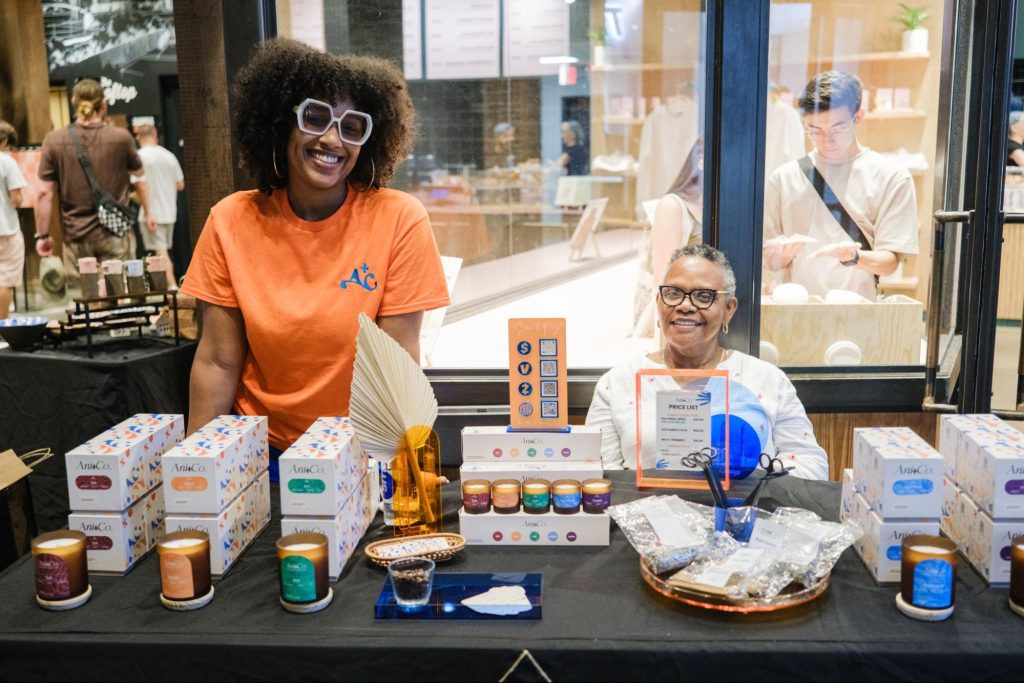 Two women behind table, selling candles