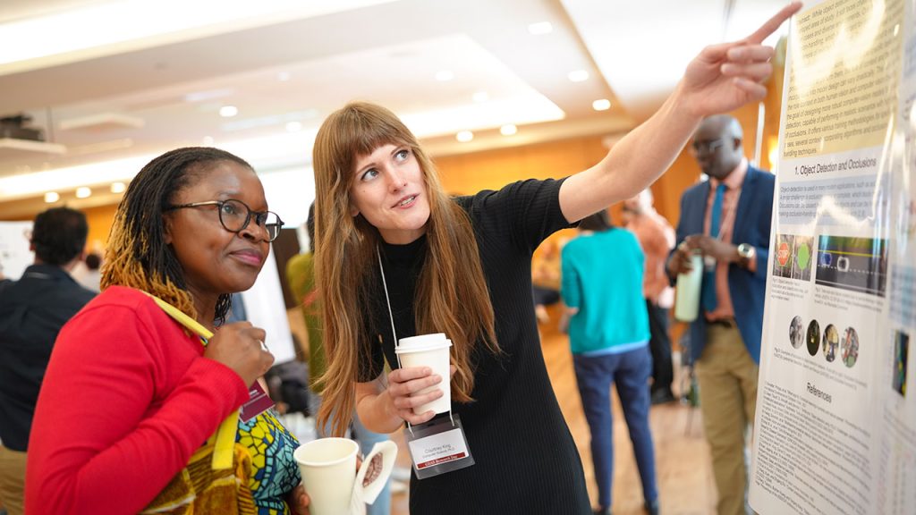 A woman points to a poster board while another looks on.