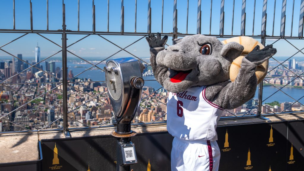 Ramses throws his hands up in front of binoculars on the Empire State Building.