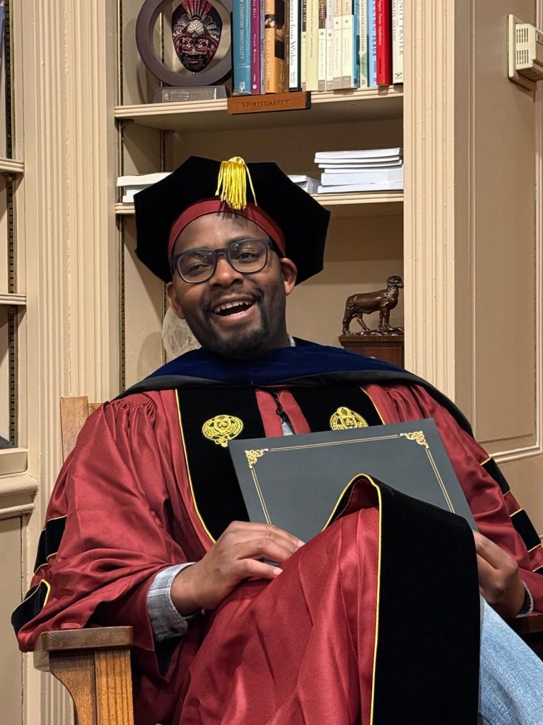 Daniel Mutale sitting in his graduation gown, holding his diploma