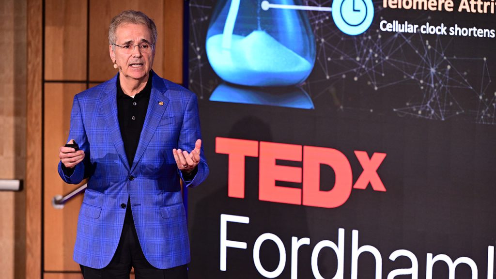 Ronald A. DePinho speaks from stage while the image of an hour glass is displayed behind him.