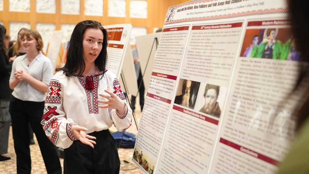 A female student standing in front of a poster board that shows her research.