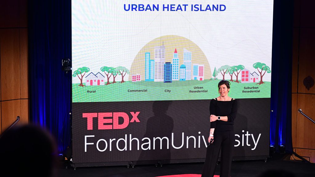 Annika Hinze speaking from a stage with a video screen behind her illustrating the heat effect on cities.