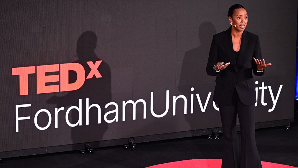Celeste Spears speaks from a stage while Tedx Fordham University is displayed behind her. 