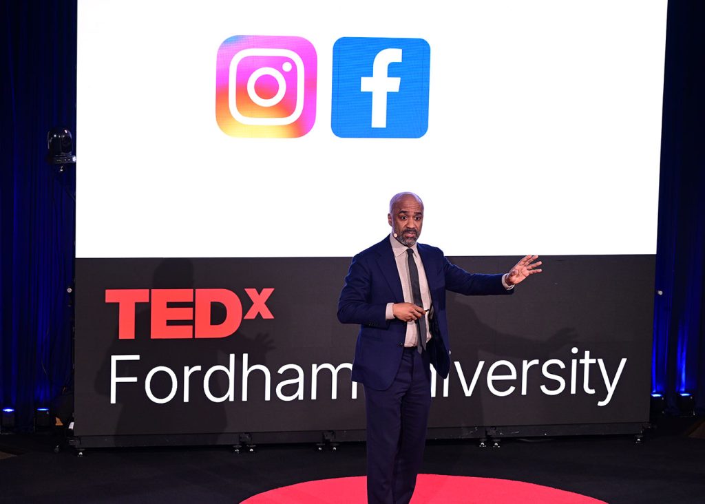 Olivier Sylvain speaks from stage while the logos of Facebook and Instagram are displayed behind him.