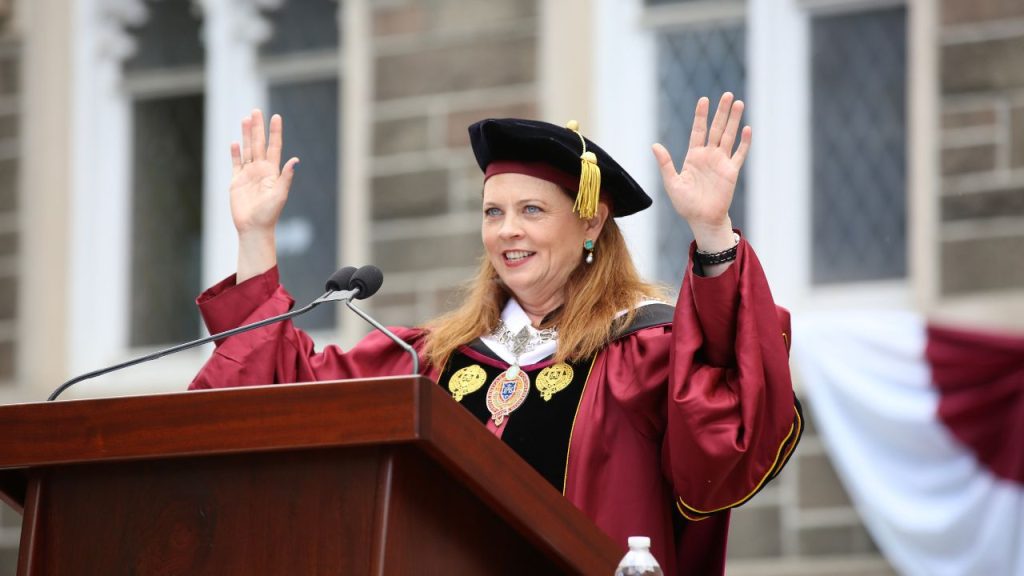 Fordham President Tania Tetlow stands with her hands in the air at a podium