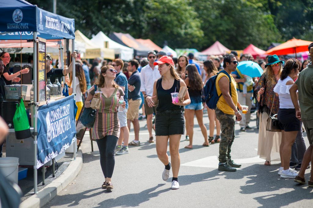 Two women walking with drinks, crowd of people and tents at Smorgasburg