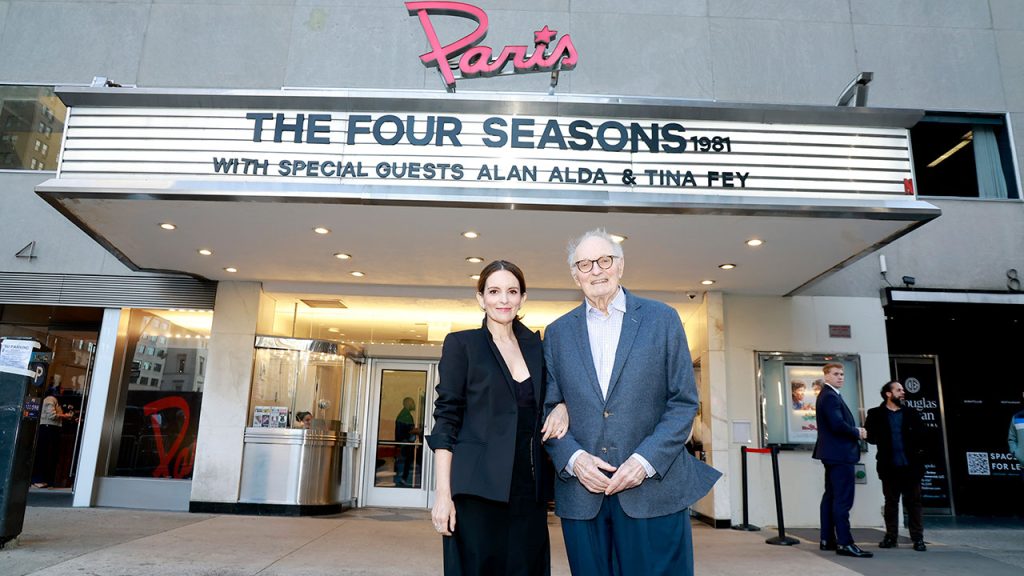 Tina Fey and Alan Alda pose for a picture in front of a billboard that says The Four Seasons