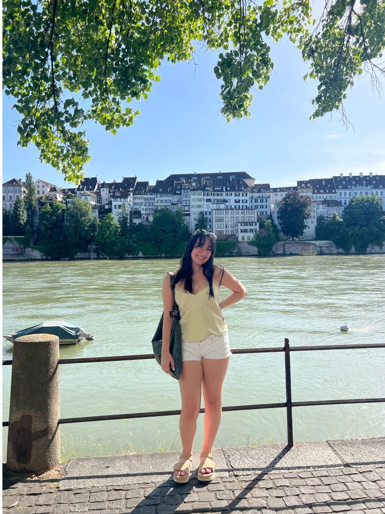 A woman stands by a river in Basel, Switzerland, representing Fordham's first ThinkSwiss scholar Julia Gudis