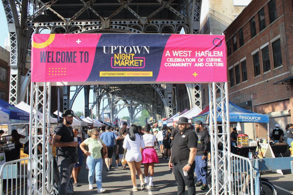 Uptown Night Market sign, with people inside and vendor tents.