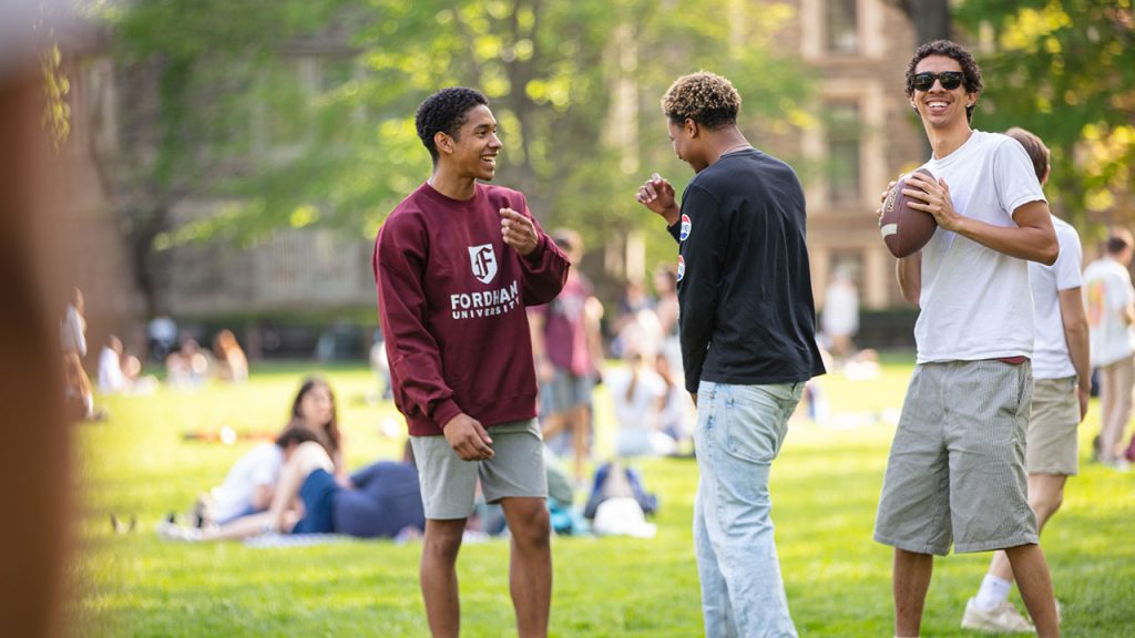 Three people standing together smiling, with one about to throw a football.