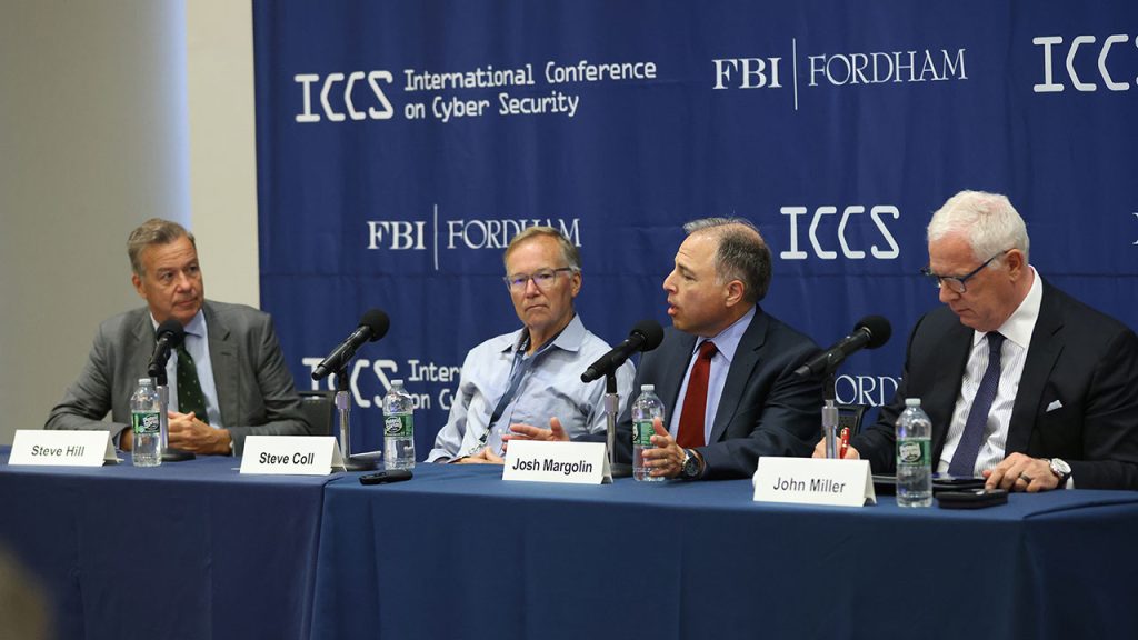 Four men seated at a table with microphones in front of them.