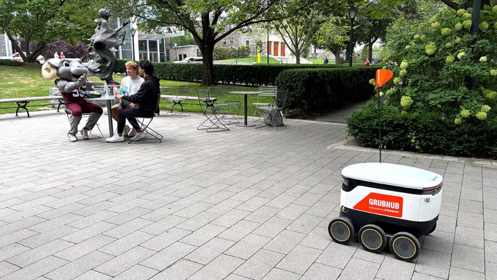 Byte to Eat: Robot Food Delivery Comes to Campus A Starship vehicle sitting next to a group of people seated at a table.