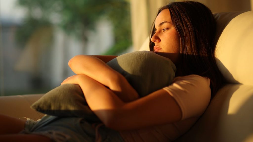 A girl sits in a chair clutching a pillow with a sad expression, representing how to deal with homesickness.