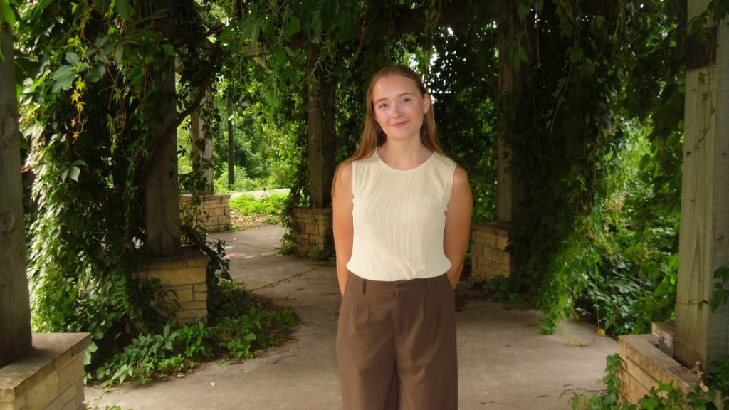 A young woman stands in a garden surrounded by greenery, representing Fordham's first Obama Voyager scholar Lillian Hertel
